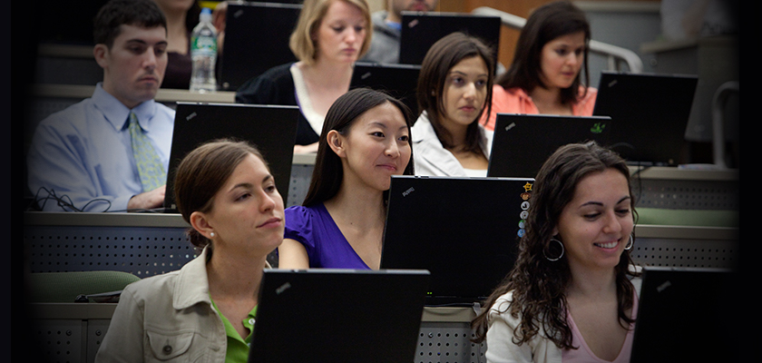 Students in lecture with laptops listening happily and smiling.