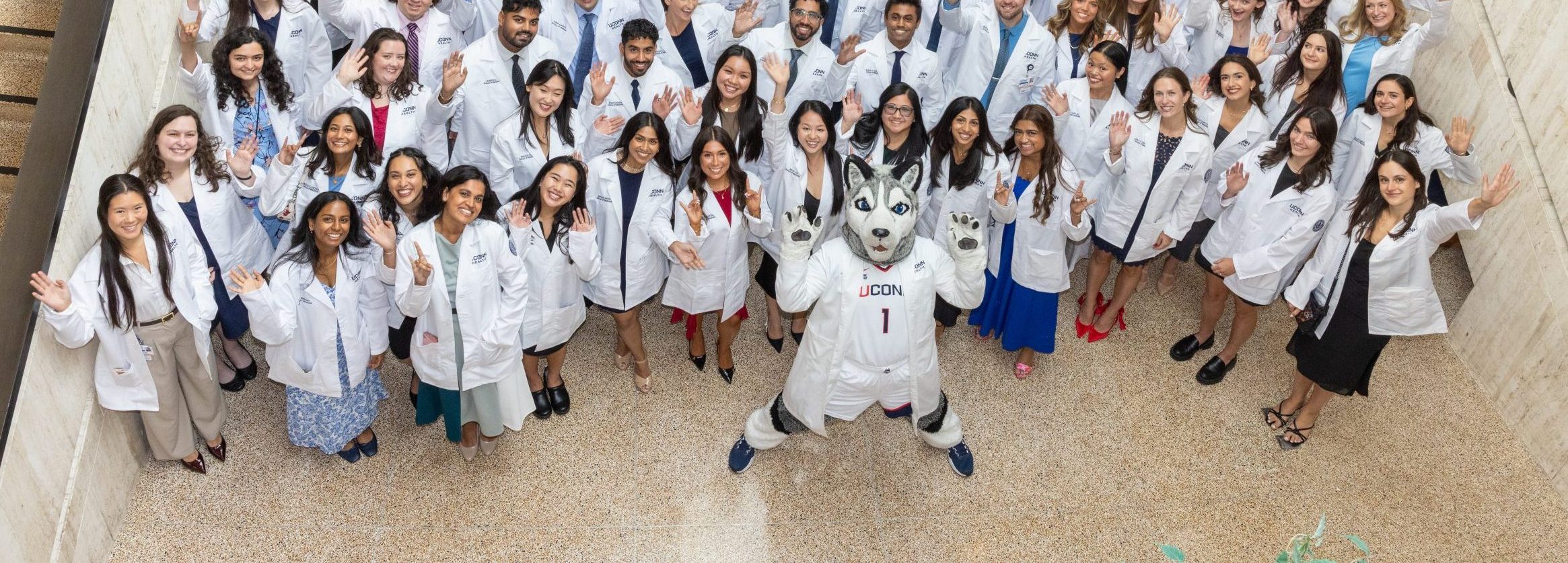 Excited looking incoming medical students get their white coats in August 2025 in the UConn Class of 2029. Group photo with Jonathan the mascot.